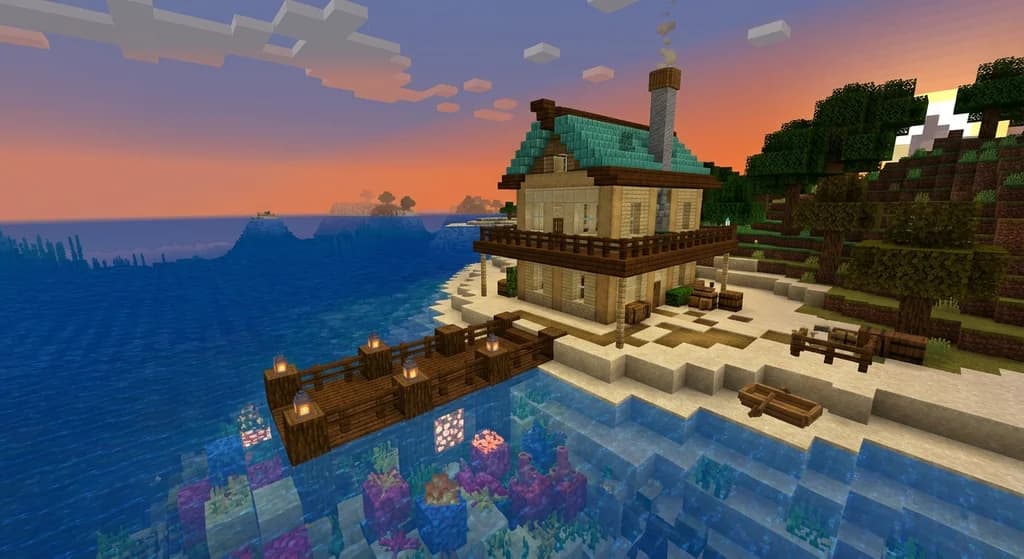 A Minecraft coastal house built from cut sandstone and prismarine with a wooden dock, sea lanterns, and coral reef in a beach biome at sunset