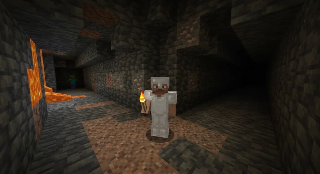 A Minecraft hardcore player in iron armor standing at a cave crossroads underground, torch in hand, two dark tunnels branching ahead with lava glow in the distance