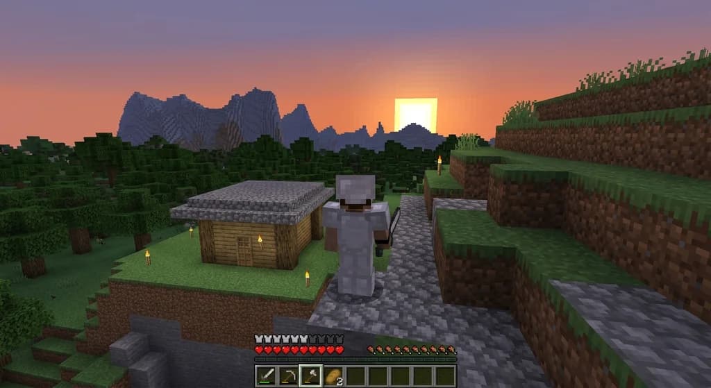 A Minecraft hardcore player in iron armor standing on a cliff at sunset above a torchlit wooden shelter, surrounded by dense oak forest and distant mountains in a survival world