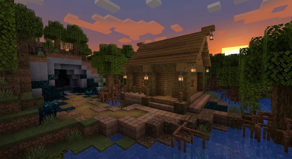 A detailed Minecraft build combining mangrove wood, mud bricks, and froglight lanterns beside a deep dark cave with sculk blocks.